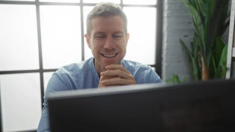 Handsome man smiling in modern office room with natural light gently illuminating his face, showing a relaxed and confident demeanor.